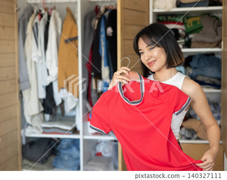 Happy young Asian girl trying to choose a dress standing by wardrobe Happy young Asian girl trying to choose a dress standing by wardrobe 140327111