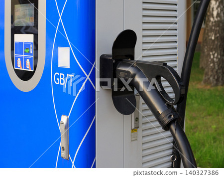 Black EV charger handle plugged into blue terminal, public electric vehicle station interface panel closeup Black EV charger handle plugged into blue terminal, public electric vehicle station interface panel closeup 140327386