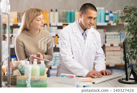 male pharmacist works at a computer against the background of a client male pharmacist works at a computer against the background of a client 140327428