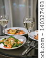 Elegant dinner for two featuring shrimp salads with almond flakes, lemon and glasses of white wine on dark reflective table in hotel room. Concept of luxury dining and romantic evening 140327493