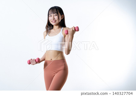 A woman lifting dumbbells to work out; dumbbell curls; female strength trainer; diagonal pose. 140327704