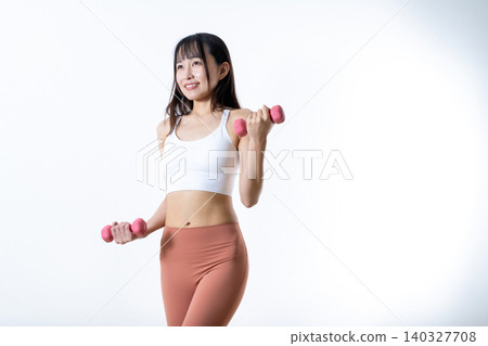 A woman lifting dumbbells to work out; dumbbell curls; female strength trainer; diagonal pose. A woman lifting dumbbells to work out; dumbbell curls; female strength trainer; diagonal pose. 140327708
