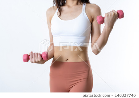 A woman lifting dumbbells to work out; dumbbell curls; female weightlifter; front view; focus on abdomen, face not visible. A woman lifting dumbbells to work out; dumbbell curls; female weightlifter; front view; focus on abdomen, face not visible. 140327740