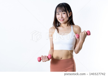 A woman lifting dumbbells to work out; dumbbell curls; female strength trainer; front view. A woman lifting dumbbells to work out; dumbbell curls; female strength trainer; front view. 140327742