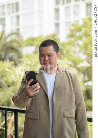 Focused plus size Isan Thai businessman using phone on balcony vertical Focused plus size Isan Thai businessman using phone on balcony vertical 140327757