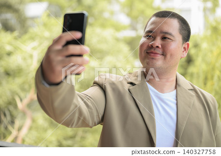 Happy plus size Isan Thai businessman taking selfie on balcony Happy plus size Isan Thai businessman taking selfie on balcony 140327758