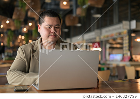 Focused plus size Isan Thai businessman using laptop at cafe Focused plus size Isan Thai businessman using laptop at cafe 140327759