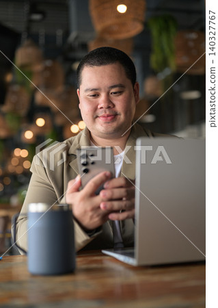 Focused plus size Isan Thai businessman using phone with laptop vertical Focused plus size Isan Thai businessman using phone with laptop vertical 140327767