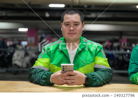 Thai delivery man from Isan looking at camera holding smartphone inside garage Thai delivery man from Isan looking at camera holding smartphone inside garage 140327796