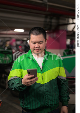 Thai delivery man from Isan checking smartphone inside motorcycle parking garage 140327800