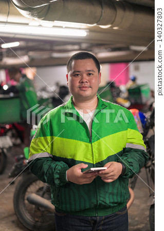 Thai delivery man from Isan looking at camera holding phone inside garage Thai delivery man from Isan looking at camera holding phone inside garage 140327803