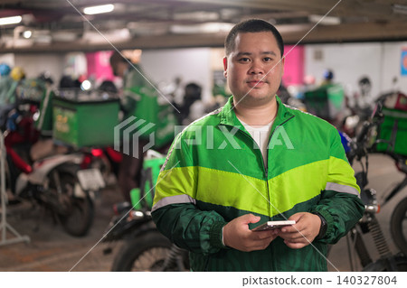 Thai delivery man from Isan holding phone in motorcycle parking garage Thai delivery man from Isan holding phone in motorcycle parking garage 140327804
