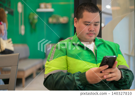 Thai delivery man from Isan checking smartphone while resting inside restaurant Thai delivery man from Isan checking smartphone while resting inside restaurant 140327810