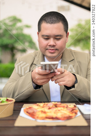 Focused plus size Isan Thai businessman using phone with pizza vertical Focused plus size Isan Thai businessman using phone with pizza vertical 140327822