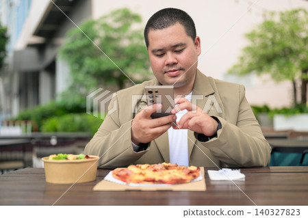 Focused plus size Isan Thai businessman texting near pizza outdoors Focused plus size Isan Thai businessman texting near pizza outdoors 140327823