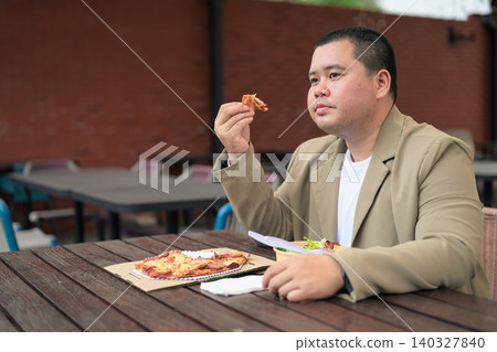 Pensive plus size Isan Thai businessman with pizza slice outdoors Pensive plus size Isan Thai businessman with pizza slice outdoors 140327840