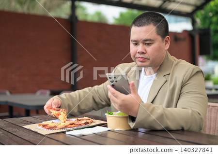 Focused plus size Isan Thai businessman using phone near pizza Focused plus size Isan Thai businessman using phone near pizza 140327841