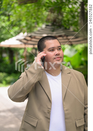 Pensive plus size Isan Thai businessman on phone call in garden vertical Pensive plus size Isan Thai businessman on phone call in garden vertical 140327882