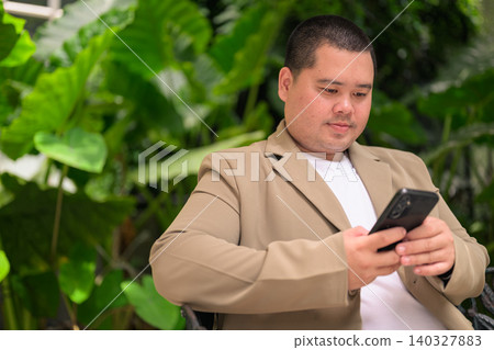 Focused plus size Isan Thai businessman using phone in garden Focused plus size Isan Thai businessman using phone in garden 140327883