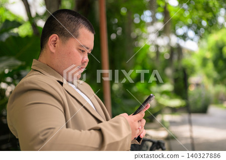 Profile of plus size Isan Thai businessman using phone in garden 140327886