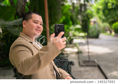 Happy plus size Isan Thai businessman taking selfie in garden 140327891