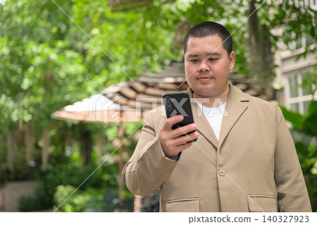 Focused plus size Isan Thai businessman using phone in garden Focused plus size Isan Thai businessman using phone in garden 140327923