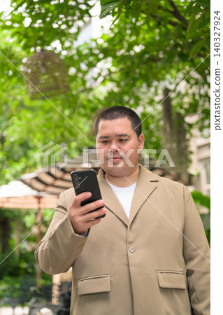 Focused plus size Isan Thai businessman using phone in garden vertical 140327924