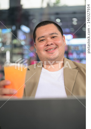 Happy plus size Isan Thai businessman holding orange juice at night cafe vertical shot Happy plus size Isan Thai businessman holding orange juice at night cafe vertical shot 140327934