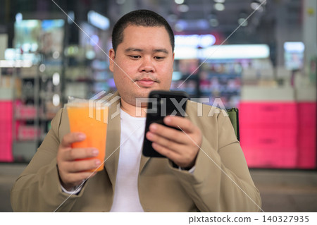 Focused plus size Isan Thai businessman using phone with orange juice Focused plus size Isan Thai businessman using phone with orange juice 140327935