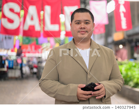Confident plus size Isan Thai businessman holding phone near sale banners Confident plus size Isan Thai businessman holding phone near sale banners 140327945