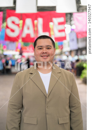 Smiling plus size Isan Thai businessman standing near sale banners vertical shot Smiling plus size Isan Thai businessman standing near sale banners vertical shot 140327947