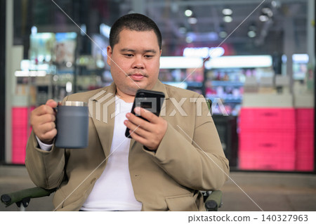 Plus size Isan Thai businessman using phone and holding a mug outdoors 140327963