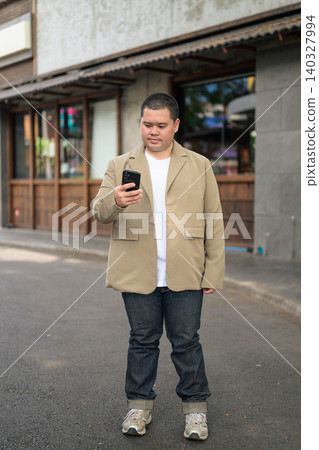 Plus size Isan Thai businessman using phone on an urban street 140327994