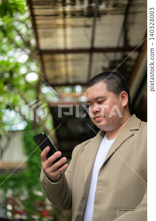 Plus size Isan Thai businessman reading text on phone at outdoor cafe 140328003