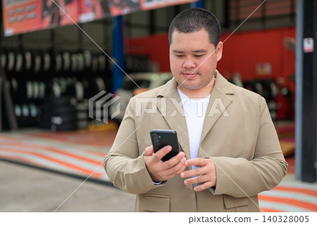 Plus size Isan Thai businessman using phone at a car service center 140328005