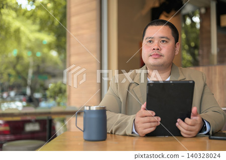 Plus size Isan Thai businessman holding tablet at an outdoor cafe Plus size Isan Thai businessman holding tablet at an outdoor cafe 140328024