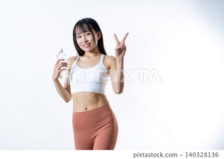 A woman with a smile and a peace sign, working out at the gym with a water bottle in her hand. 140328136