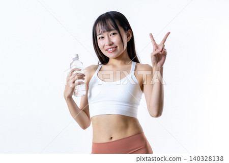 照片中，一位正在健身房鍛鍊的女士面帶微笑，比出「V」字手勢，手裡拿著水瓶。照片的焦點是一位熱衷於肌肉訓練的女性。 140328138