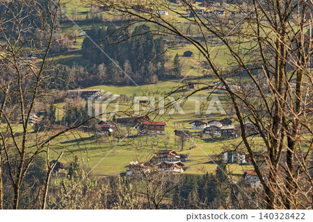 Looking trough tree branches on a village in a valley Looking trough tree branches on a village in a valley 140328422