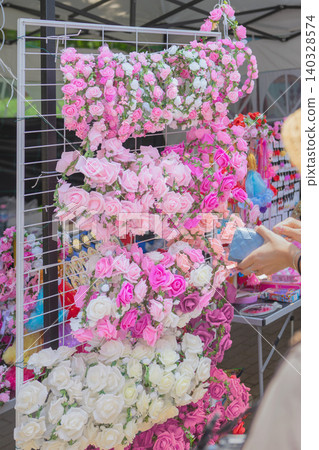 Rose floral accessories hang on display rack at outdoor market stall during Rose Festival in Bulgaria. Rose festival market with souvenir shopping, craft stall, flower display Rose floral accessories hang on display rack at outdoor market stall during Rose Festival in Bulgaria. Rose festival market with souvenir shopping, craft stall, flower display 140328574