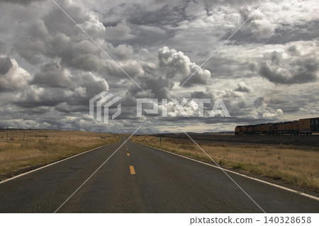 Freight train moving along lonely road under cloudy sky Freight train moving along lonely road under cloudy sky 140328658