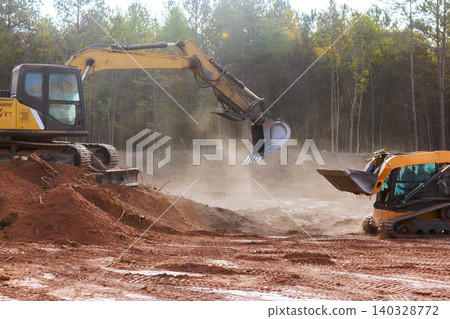 Heavy machinery digs moves dirt at construction site surrounded by trees in forested area Heavy machinery digs moves dirt at construction site surrounded by trees in forested area 140328772