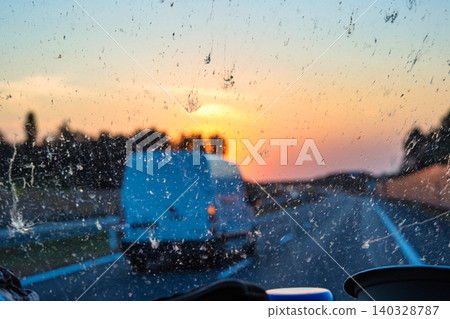 Sunset view through a dirty car windshield on the highway with a van in motion, focusing on travel, visibility, and road safety concerns. Transportation, logistics, road traffic. Copy space Sunset view through a dirty car windshield on the highway with a van in motion, focusing on travel, visibility, and road safety concerns. Transportation, logistics, road traffic. Copy space 140328787