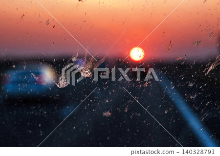 Blurry highway through a smudged dirty car windshield, affecting visibility during orange sunset, emphasizing traffic safety concerns and the importance of clean glass for safe travel. Blurry highway through a smudged dirty car windshield, affecting visibility during orange sunset, emphasizing traffic safety concerns and the importance of clean glass for safe travel. 140328791