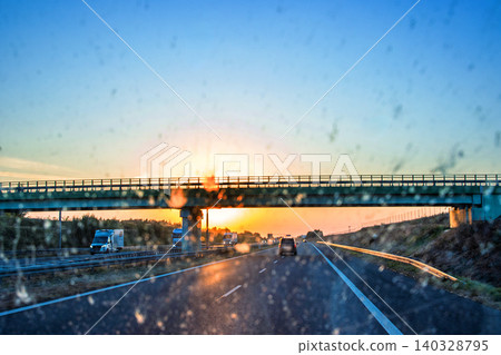 Highway and bridge at sunset through a dirty windshield, emphasizing road safety and the challenges of visibility while driving on long journeys. Transportation, logistics, road traffic. Copy space Highway and bridge at sunset through a dirty windshield, emphasizing road safety and the challenges of visibility while driving on long journeys. Transportation, logistics, road traffic. Copy space 140328795