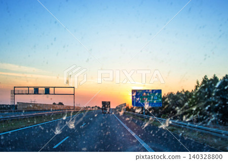 Blurry windshield sunset scene on a highway with cars and navigating signs, symbolizing navigation, transportation, logistics, road traffic. Poznan, Lodz, Wroclaw, Poland, A2, E30. Copy space Blurry windshield sunset scene on a highway with cars and navigating signs, symbolizing navigation, transportation, logistics, road traffic. Poznan, Lodz, Wroclaw, Poland, A2, E30. Copy space 140328800