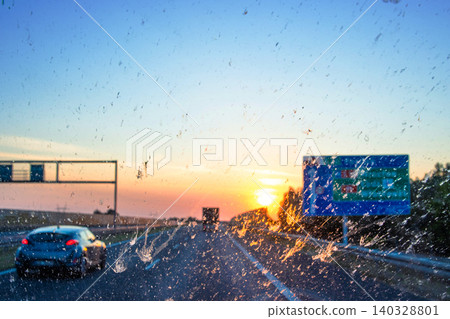 Blurry windshield sunset scene on a highway with cars and navigating signs, symbolizing navigation, transportation, logistics, road traffic. Poznan, Lodz, Wroclaw, Poland, A2, E30. Copy space Blurry windshield sunset scene on a highway with cars and navigating signs, symbolizing navigation, transportation, logistics, road traffic. Poznan, Lodz, Wroclaw, Poland, A2, E30. Copy space 140328801