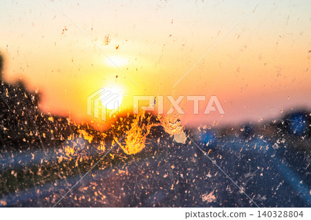 Blurry highway through a smudged dirty car windshield, affecting visibility during sunset, emphasizing highway traffic safety concerns and the importance of clean glass for safe travel. Blurry highway through a smudged dirty car windshield, affecting visibility during sunset, emphasizing highway traffic safety concerns and the importance of clean glass for safe travel. 140328804