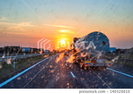 Sunset highway view through a dirty windshield with a tanker truck ahead, showing riving conditions, vehicle maintenance, and scenic road safety, and visibility challenges. Copy space Sunset highway view through a dirty windshield with a tanker truck ahead, showing riving conditions, vehicle maintenance, and scenic road safety, and visibility challenges. Copy space 140328810