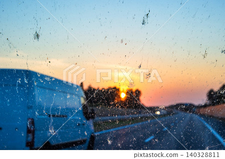 Sunset view through a dirty car windshield on the highway with a van in motion, focusing on travel, visibility, and road safety concerns. Transportation, logistics, road traffic. Copy space Sunset view through a dirty car windshield on the highway with a van in motion, focusing on travel, visibility, and road safety concerns. Transportation, logistics, road traffic. Copy space 140328811